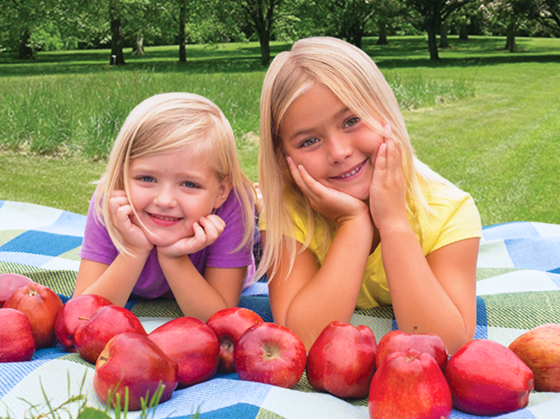 Two young girls with apples on a blanket.